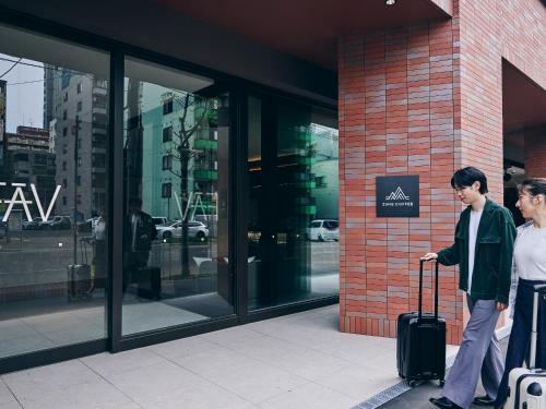 two people standing outside of a building with their luggage at FAV LUX Sapporo Susukino in Sapporo