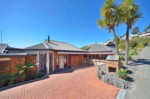 a house with a brick driveway and palm trees at The Cliffs - Nelson Waterfront Home in Nelson