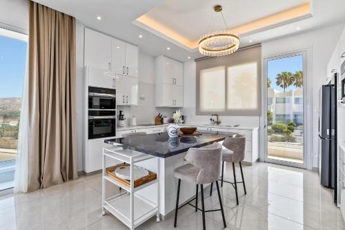 a kitchen with white cabinets and a table with stools at Olymp White Palace - The Ultra Luxury Beach House in Kissonerga