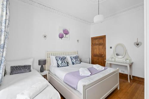 a white bedroom with two beds and a mirror at Beach Walk Apartment in Broughty Ferry