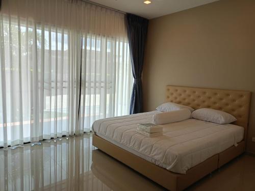 a bedroom with a bed with white sheets and large windows at Anchan Gardens Pool Villa 23 in Hua Hin