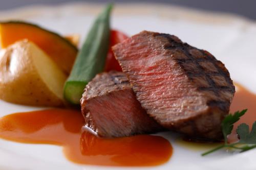a piece of meat on a plate with fruits and vegetables at Yatsugatake Kogen Lodge in Minamimaki