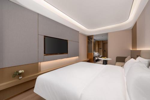 a bedroom with a white bed and a flat screen tv at Platon International Apartment - Lunjiao Metro Station Store in Shunde