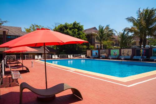 a swimming pool with a red umbrella and chairs and tables at Hapuwani Village Lodge in Mulanje