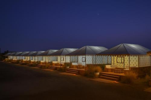 a row of buildings with tables and umbrellas at night at The Carvaans Resort-Luxury Desert Camp Jaisalmer in Jaisalmer