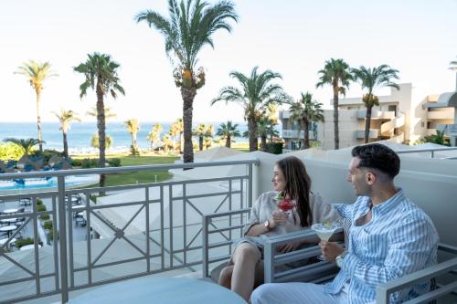 a man and a woman sitting on a balcony with drinks at Rodos Palladium Leisure & Wellness in Faliraki