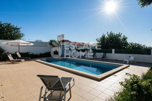 a swimming pool with chairs and an umbrella on a patio at Villa Sunset Lovers in Alcantarilha