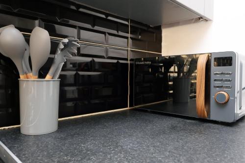 a cup of kitchen utensils in front of a microwave at Lovely 3-Bed in Scenic Aberdare! in Aberdare