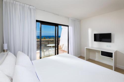 a white bedroom with a bed and a balcony at Sol Fuerteventura Jandia - All Suites in Morro del Jable