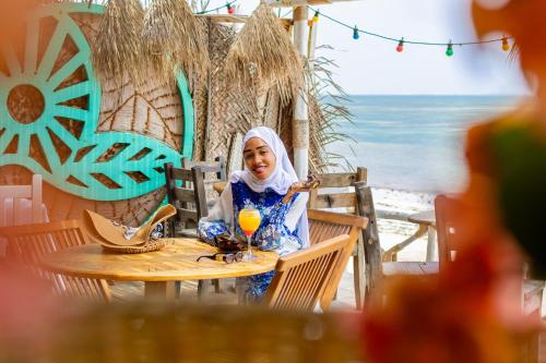 a woman sitting at a table on the beach at ZAN Beach House in Bwejuu