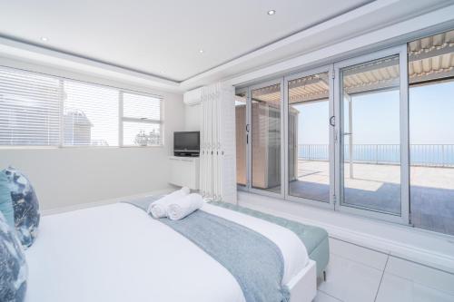 a white bedroom with a bed and large windows at 122 Camarque-Lavish lookout Penthouse in Umdloti