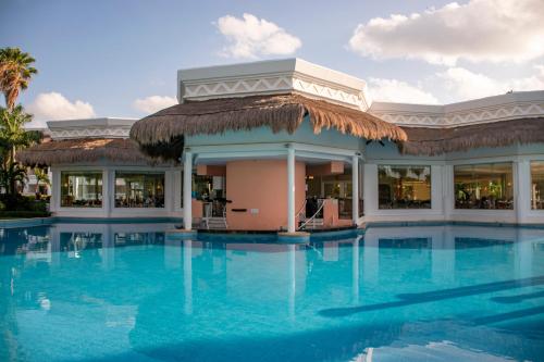 a swimming pool with a building with a straw roof at Grand Sunset Princess - All Inclusive in Playa del Carmen