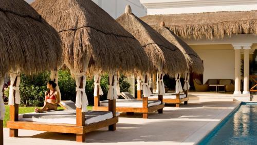 a row of beds with straw umbrellas next to a pool at Grand Riviera Princess - All Inclusive in Playa del Carmen