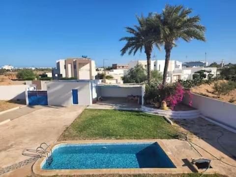 a backyard with a swimming pool and a palm tree at Appartment, séjour Djerba 2 in Arkou