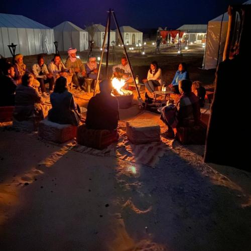 a group of people sitting around a fire at night at Merzouga tente luxury in Merzouga