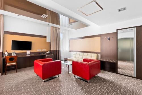 a hotel room with two red chairs and a television at Park Hotel Diament Zabrze - Gliwice in Zabrze