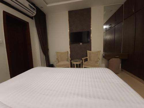 a bedroom with a bed and two chairs and a tv at Aspire Lodge, G11 Islamabad - A Family Guest House & Hotel in Islamabad