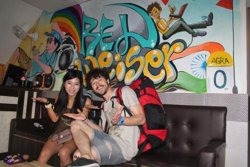 a man and woman sitting on a couch in front of a mural at Bedweiser Backpackers Hostel in Agra