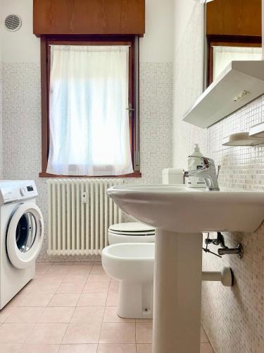 a bathroom with a sink and a toilet and a washing machine at Condominio Tirrenia 5 in Lignano Sabbiadoro