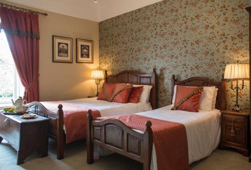 two beds in a hotel room with floral wallpaper at Raheen House Hotel in Clonmel