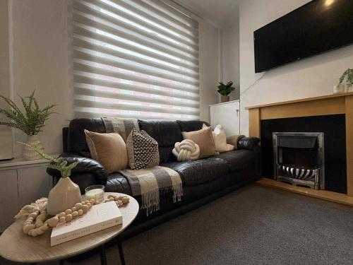 a living room with a black leather couch and a fireplace at Wallasey Home - 2 Min to Liverpool Ferry Seacombe, Beach & Free Parking in Wallasey