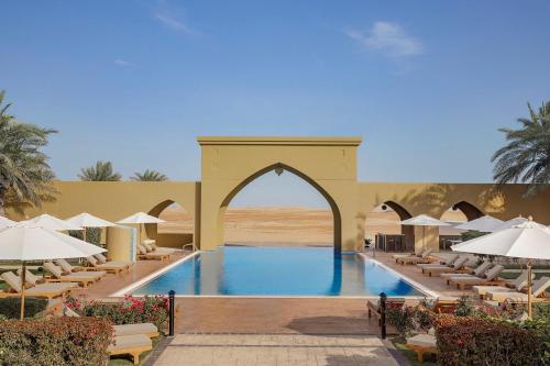 a pool at a resort with chairs and umbrellas at Aldhafra Desert Resort, Vignette Collection by IHG in Madīnat Zāyid
