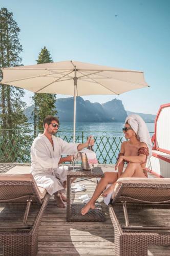 a man and woman sitting under an umbrella on a deck at Hotel Vitznauerhof - Lifestyle Hideaway at Lake Lucerne in Vitznau