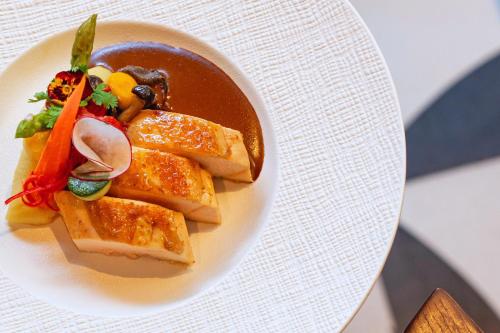 a white plate with a bowl of food on a table at Hotel Indigo Saigon the City by IHG in Ho Chi Minh City
