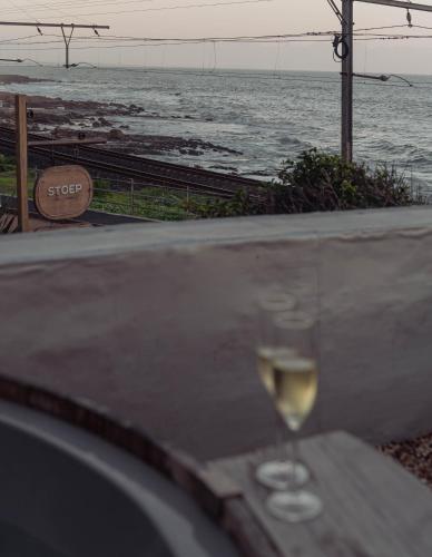 a glass of wine sitting on a table near the ocean at Stoep By Ideas Cartel in Kalk Bay