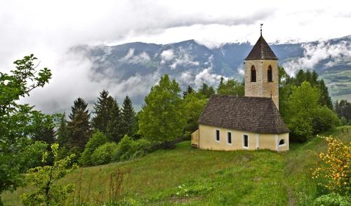 an old church on a hill with a mountain at SAN PIETRO DOLOMITI Small Budget Hotel in Ortisei