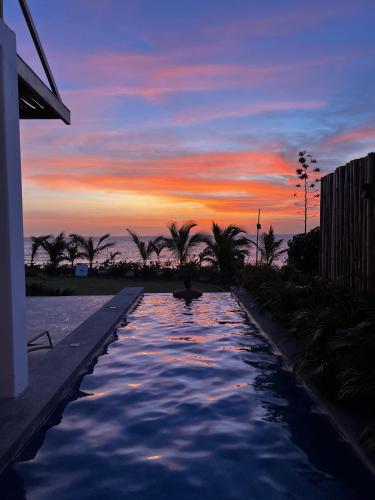 a swimming pool with a sunset in the background at Gaia - Casa de Playa in Canoas de Punta Sal