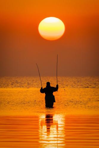 a man is standing in the water with two fishing rods at Casa Dochia in Sfântu Gheorghe