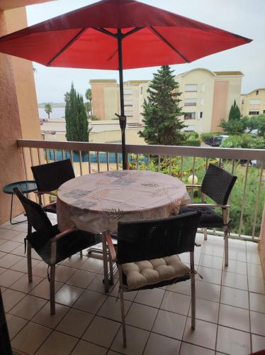 a table and chairs with a red umbrella on a balcony at Le Thalassa I appartement T2 en bord de plage et du Port in Gruissan