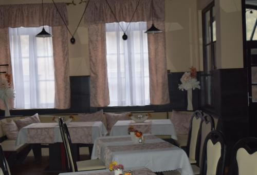 un comedor con mesas y sillas blancas y ventanas en Ring Penzión, en Komárno