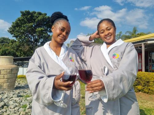 two women in white lab coats holding glasses of wine at La Exotica Lodge & Spa in Rustenburg