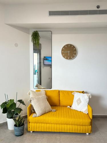 a yellow couch in a room with a mirror and a clock at Beach Suite Israel, Beachfront Suite, Indoor Pool, Gym Spa ביץ סוייט ישראל בריכה מקורה, חדר כושר וספא בבניין in Ashqelon