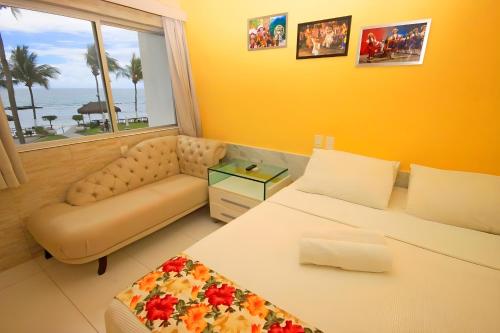 a bedroom with a bed and a couch and a window at FLATS VISTA MAR e FRENTE MAR NA PRAIA DOS CARNEIROS in Praia dos Carneiros