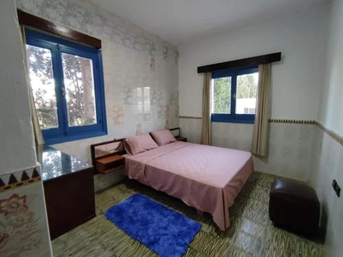 a small bedroom with a bed and two windows at Afriquia Star in Oulad Akkou