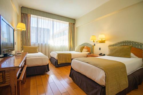 a hotel room with two beds and a television at Hotel Frontera Clásico in Temuco