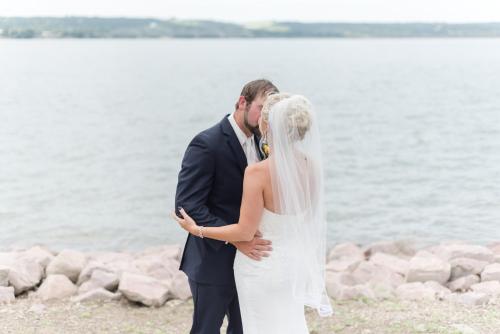a bride and groom kissing next to the water at Cedar Shore Resort in Oacoma