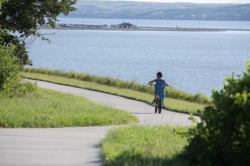 a young boy riding a bike on a path near the water at Cedar Shore Resort in Oacoma