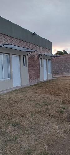a brick building with white doors and a yard at OMA Departamentos por día -1 in General Acha