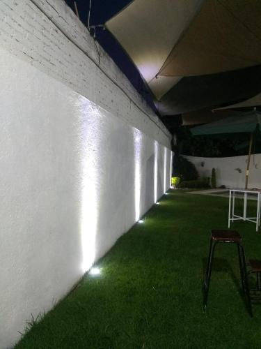a room with green grass and a white wall with lights at Hermosa casa residencial alberca propia climatizada in Cuautla Morelos