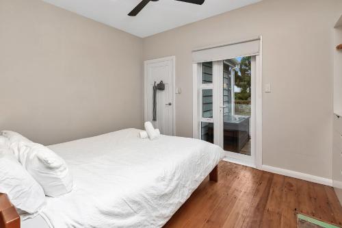 a white bedroom with a bed and a sliding glass door at Chic Whangarei Retreat - 10 min Walk to CBD in Whangarei