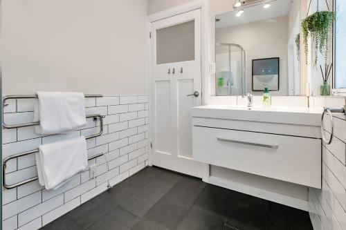 a white bathroom with a sink and a mirror at Chic Whangarei Retreat - 10 min Walk to CBD in Whangarei