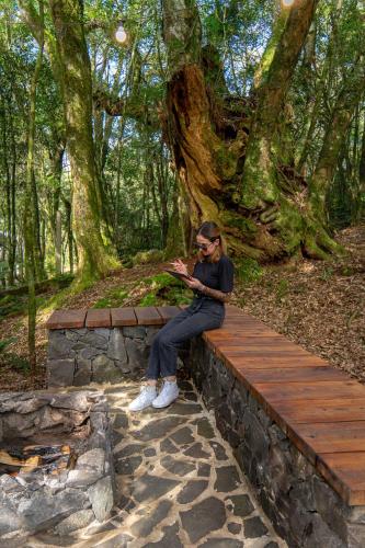 a woman sitting on a wooden bench in a forest at Cabana na Serra Rs in São Francisco de Paula