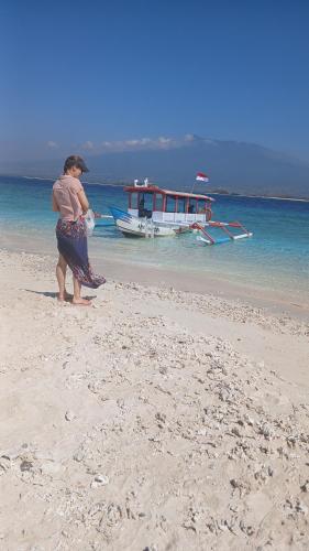 a woman standing on a beach with a boat in the water at Green Escape in Tetebatu