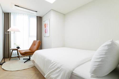 a white bedroom with a bed and a chair at Brown Suites Busan Station in Busan