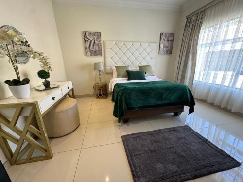a bedroom with a bed with a green blanket and a desk at Orkney Villa in Klerksdorp