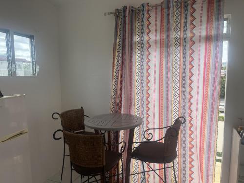 a table and chairs in a room with a curtain at Appartement Coquelicot à 5 min du CENTRE VILLE FDF in Fort-de-France